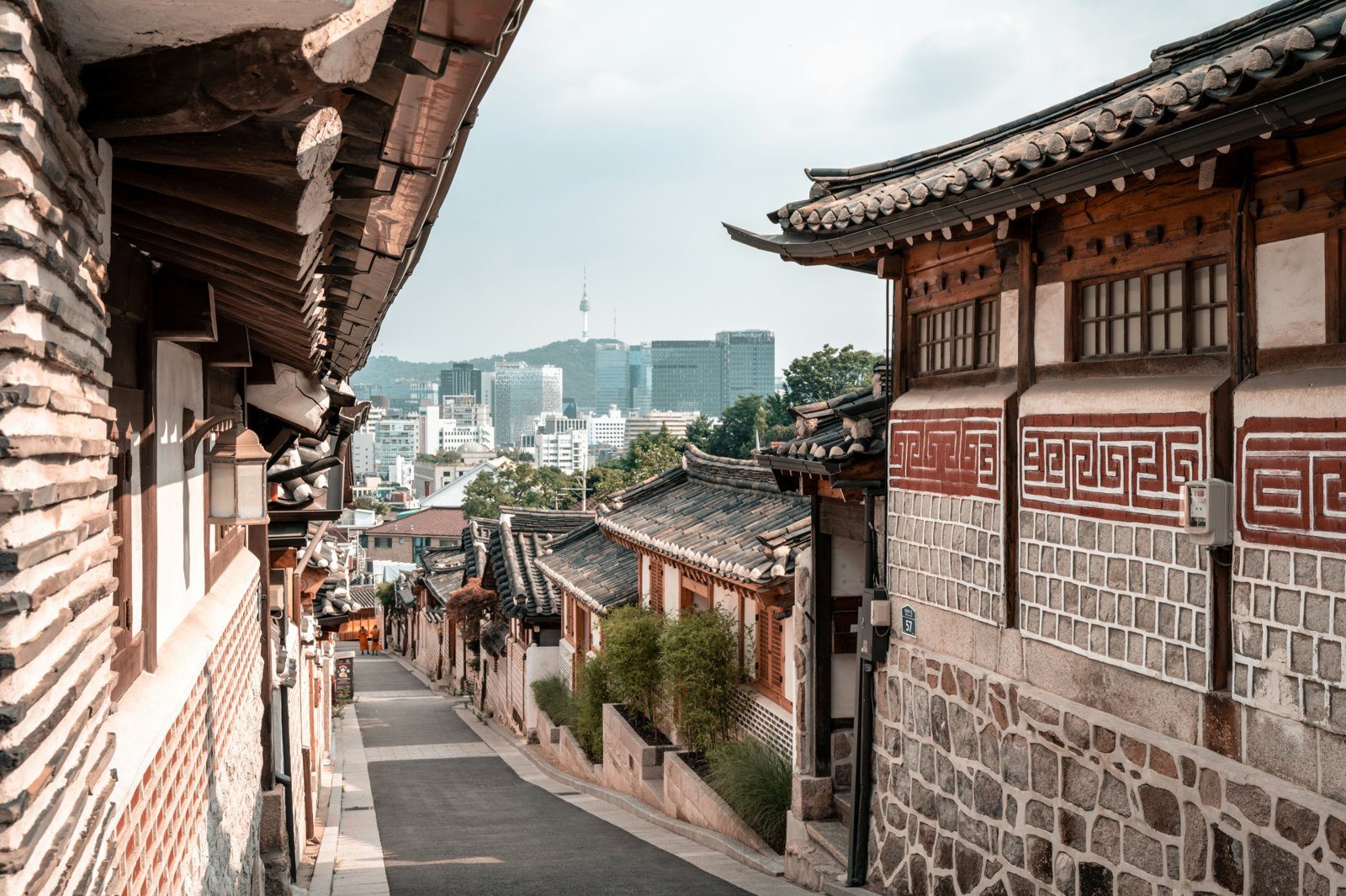 The famous hanok-lined alley of Bukchon Hanok Village with the Seoul skyline beyond