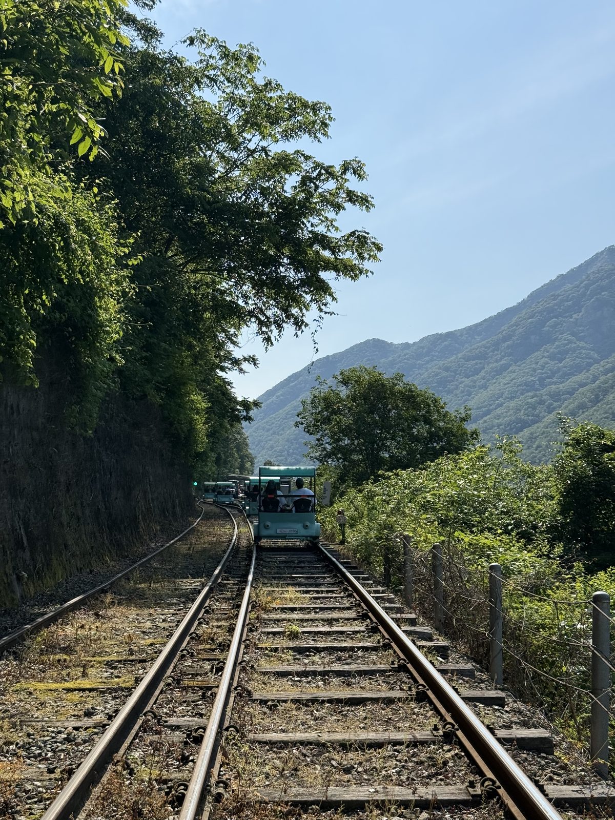 Rail bike tracks running between a rock face and the hills near Gangchon, with a rail bike ahead on the line