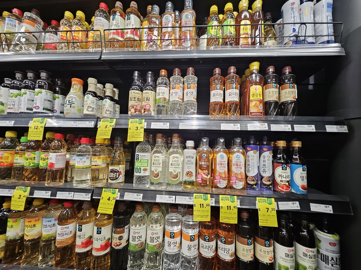 Supermarket shelves of Korean fish sauces and briny condiments: kanari and myeolchi aekjeot (sand lance and anchovy sauce), tsuyu and syrups.