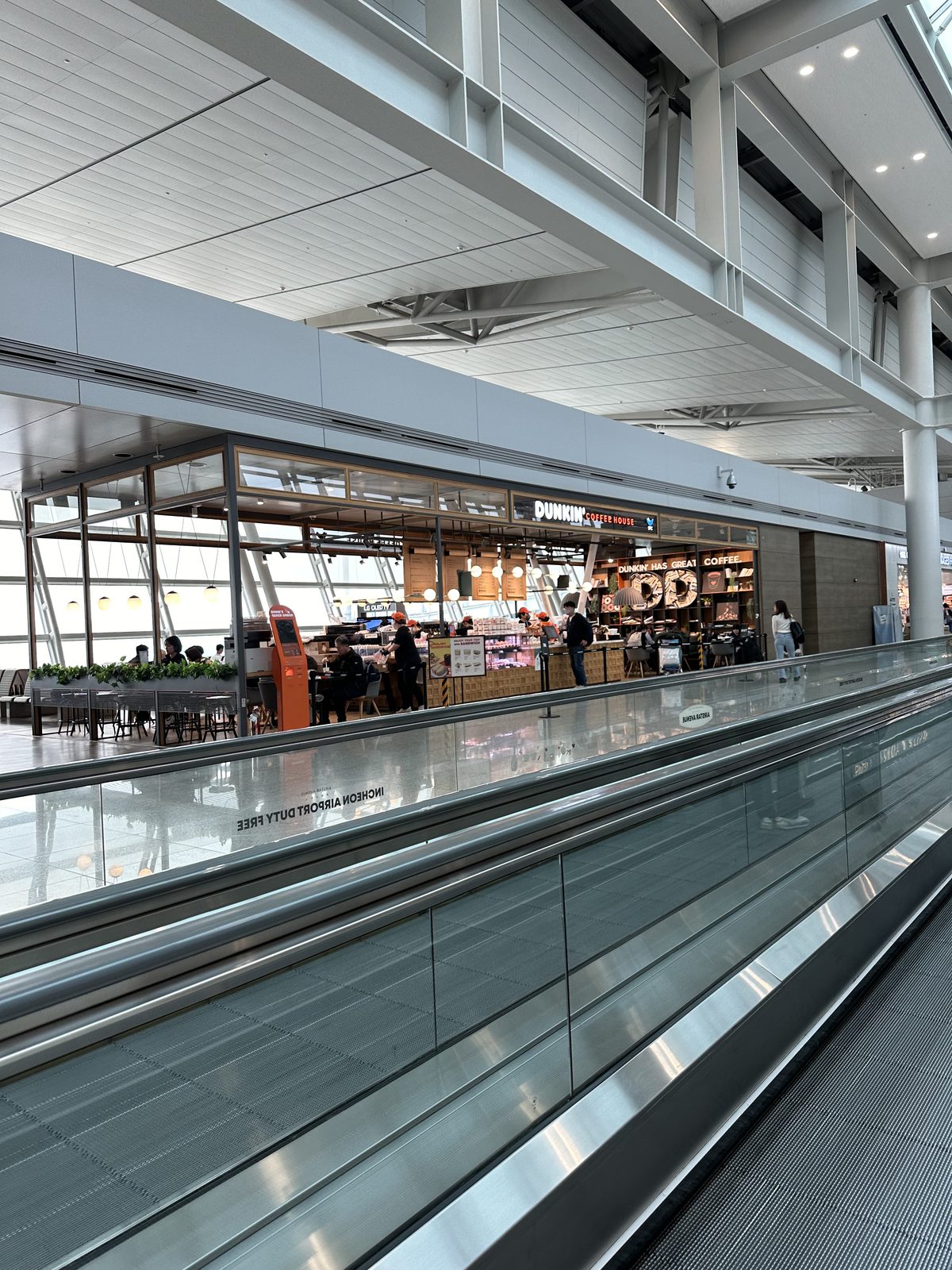 A long moving walkway inside Incheon Airport Terminal 1, with shops and a food court alongside it