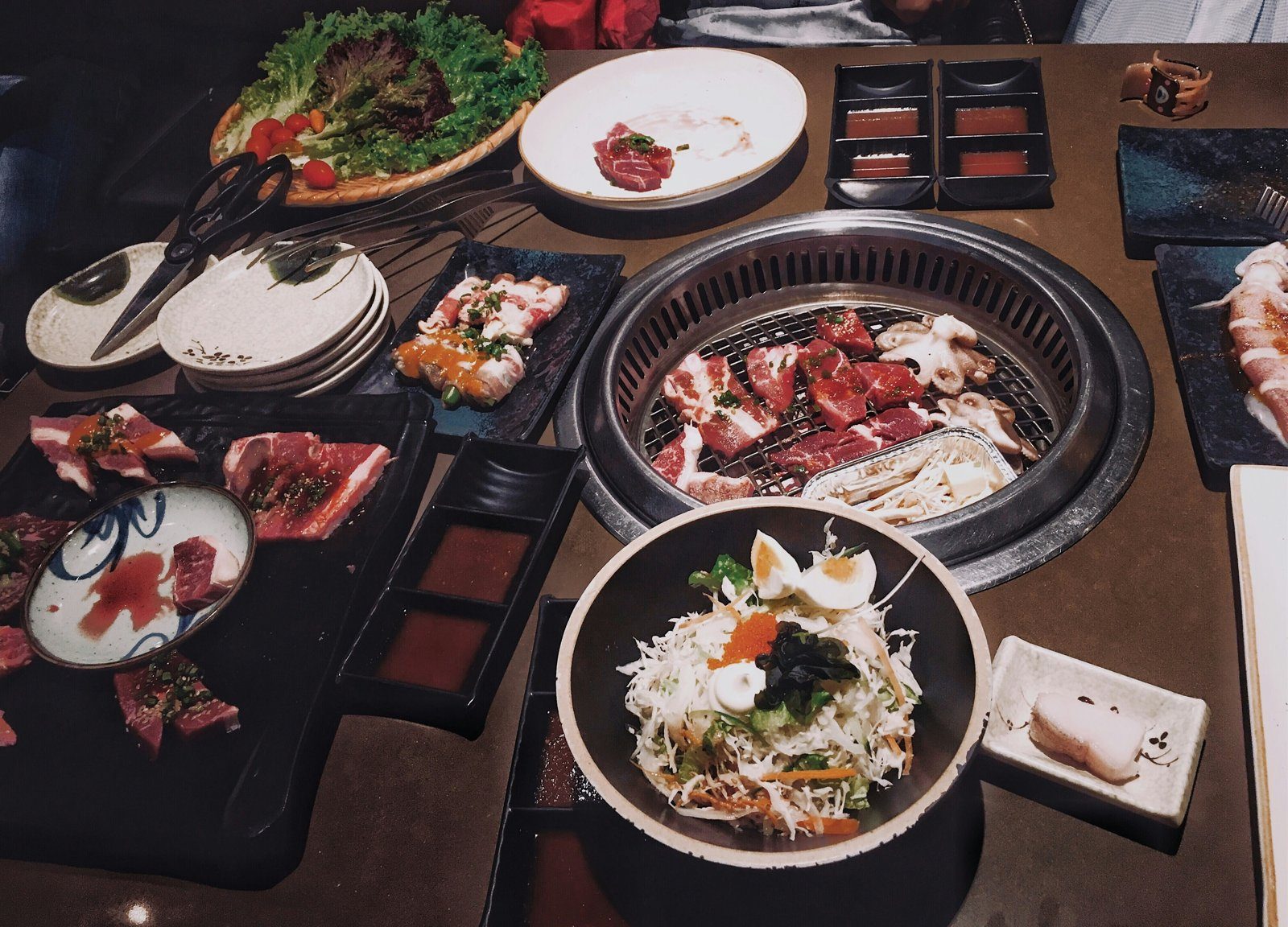 A Korean BBQ table spread with meat grilling in the centre and banchan side dishes