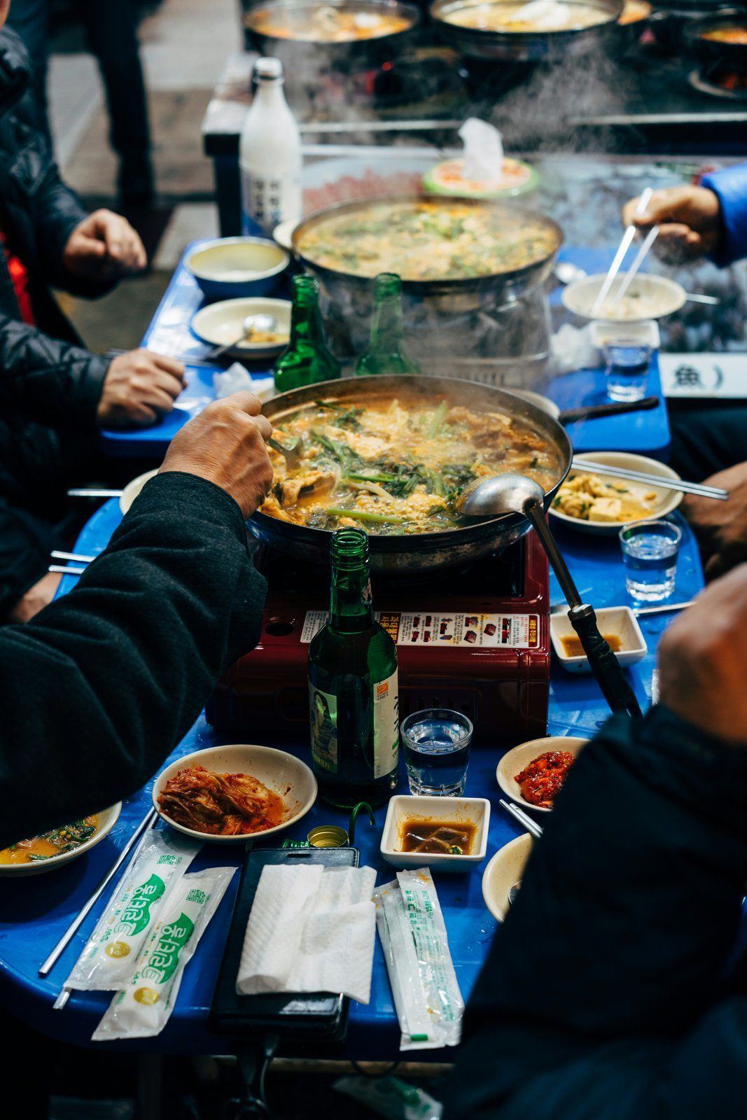 People eating stew and drinking soju at an outdoor Korean market eatery