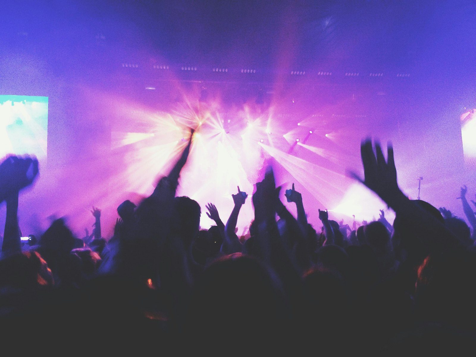 A K-pop concert crowd with hands raised and purple stage lights