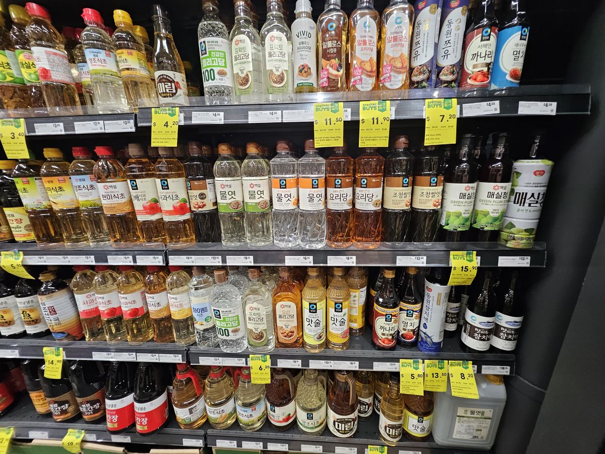 Supermarket shelves of Korean cooking wines, mirin, syrups and plum extracts in plastic bottles.