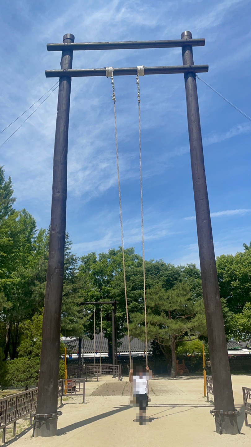 The tall wooden Chunhyang swing at Gwanghalluwon Garden in Namwon, with a visitor riding it