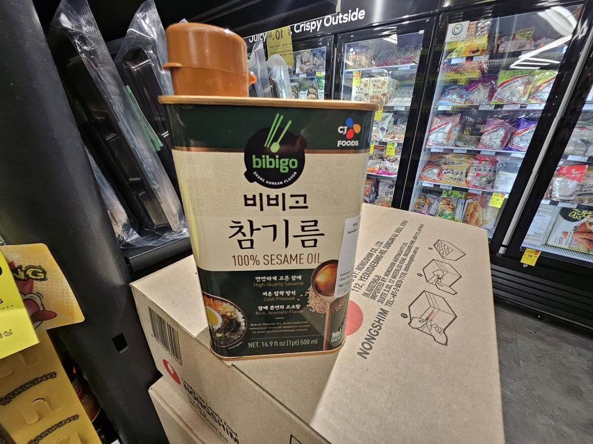 A gold tin of Korean 100% sesame oil on a store shelf, with a similar tin of perilla oil sold beside it.