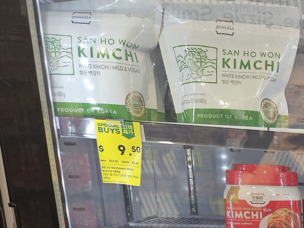 Close-up of packaged white kimchi in a supermarket fridge with a label reading WHITE KIMCHI / MILD & VEGAN, product of Korea.