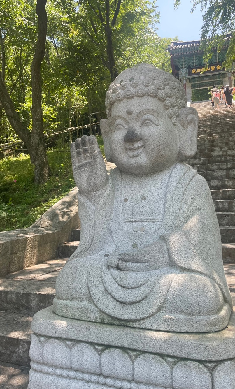 A small smiling stone Buddha with a raised hand beside the steps at Hyangiram